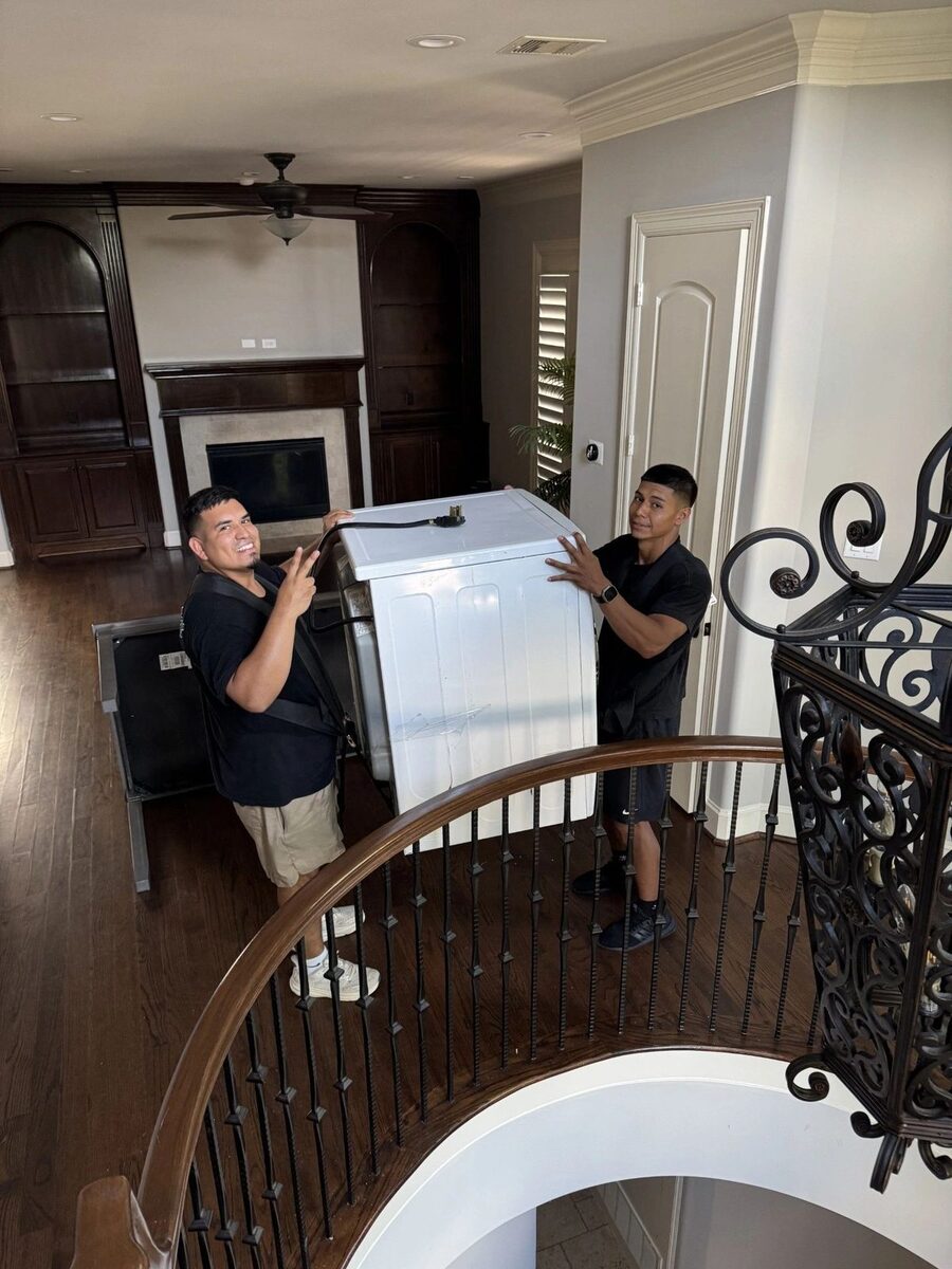 Two PRO MOVE crew members carefully carrying a heavy piece up a staircase inside a home